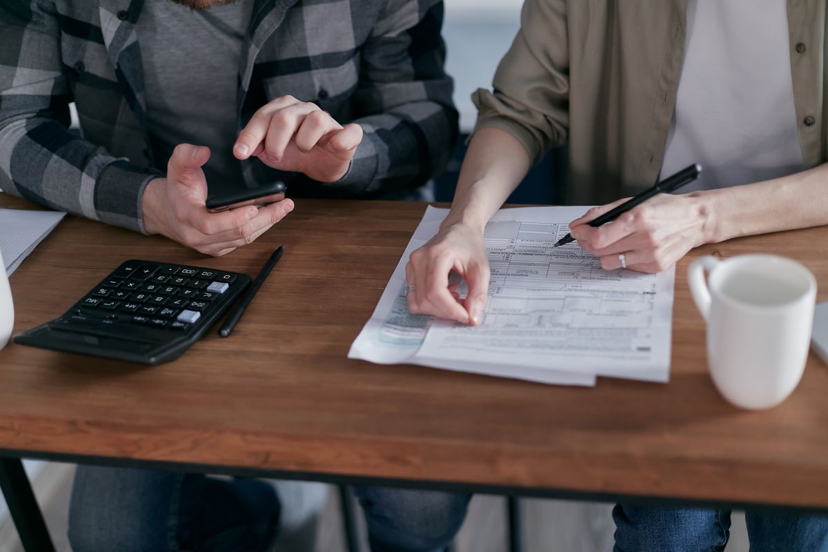 Two people reviewing financial paperwork beside a calculator at a desk.