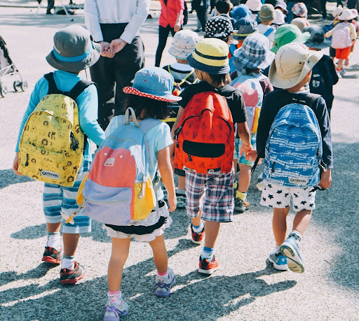 Young children walking together with school backpacks Group of young children wearing backpacks and hats walking together outdoors, representing early childhood routines, transitions, and daily structure.