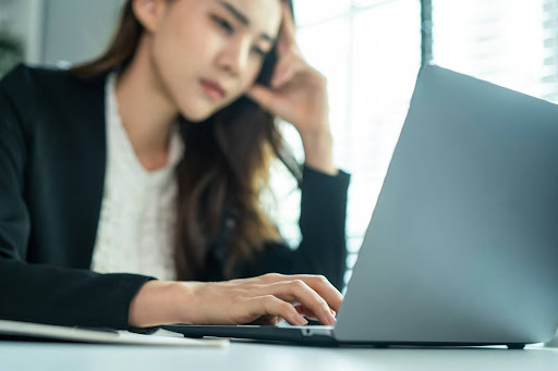 Focused professional working on a laptop in a modern workspace Professional woman concentrating while working on a laptop at a desk, representing cognitive focus, mental effort, and modern knowledge-based work.