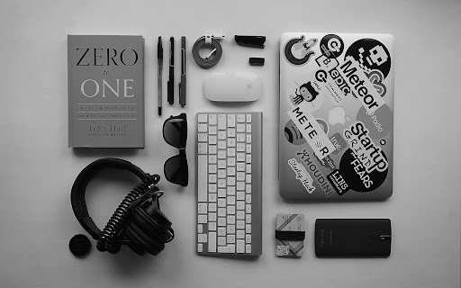 Minimalist desk setup with modern work accessories Flat lay of a modern workspace featuring a laptop with stickers, keyboard, headphones, notebook, and everyday professional accessories on a clean desk.