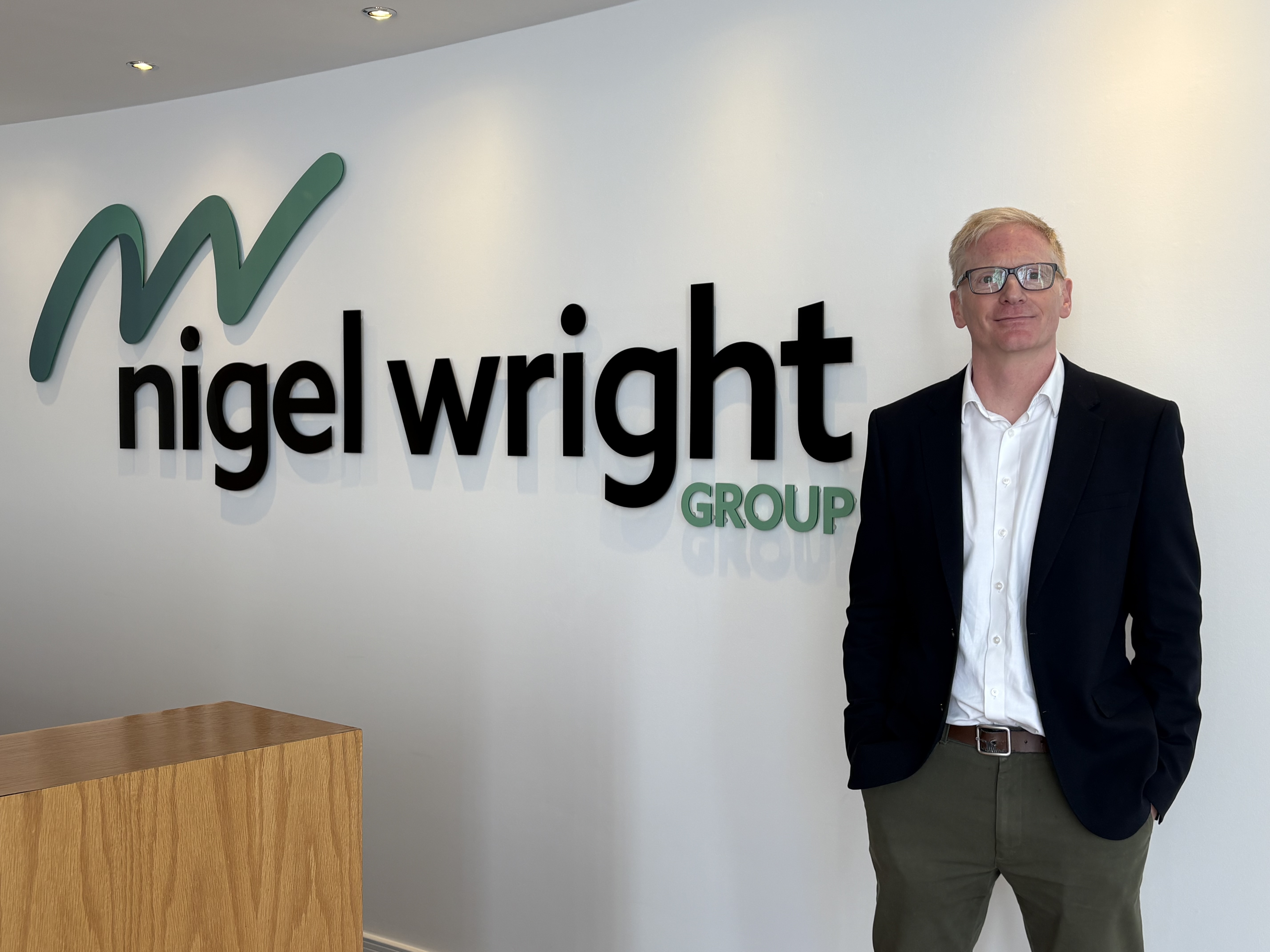 Mark Simpson standing beside the Nigel Wright Group sign in an office reception.