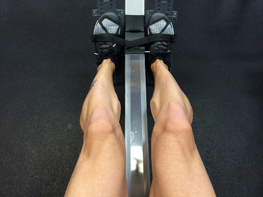 Lower body engagement during a rowing machine workout Person using a rowing machine at the gym, showing leg muscles engaged during a fitness and endurance workout.