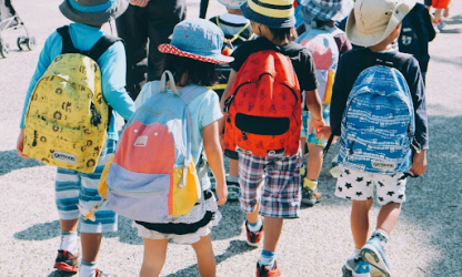 Group of young children wearing backpacks and hats walking together outdoors, representing early childhood routines, transitions, and daily structure.