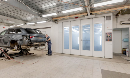 Mechanic working beside a raised car in an automotive repair workshop.