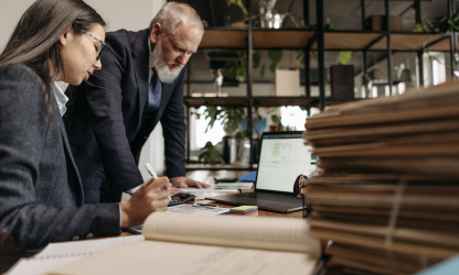 Two colleagues review documents together at an office desk