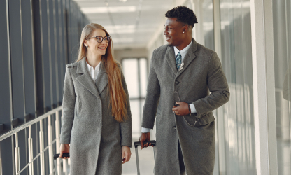 Two business travellers walking through an airport with wheeled luggage; illustrative stock photograph.