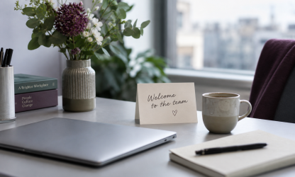 A prepared welcome desk with a laptop, notebook, coffee, flowers and a card saying Welcome to the team. Generated concept image.