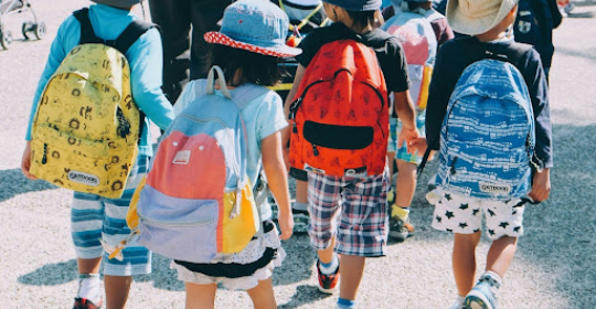 Group of young children wearing backpacks and hats walking together outdoors, representing early childhood routines, transitions, and daily structure.