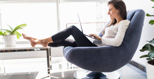 Person working on a laptop while sitting comfortably in a modern chair at home, representing remote work, everyday comfort, and balanced work-from-home routines.