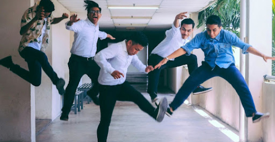 Group of colleagues jumping and laughing together in a hallway, representing workplace energy, team bonding, and playful company culture
