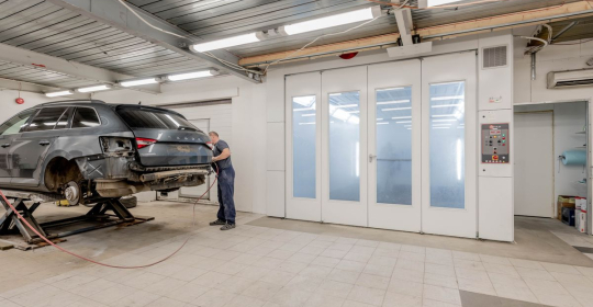 Mechanic working beside a raised car in an automotive repair workshop.