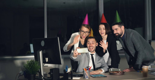 Colleagues celebrating a personal milestone at work Group of coworkers wearing party hats and smiling around a desk, celebrating a workplace milestone in a modern office environment