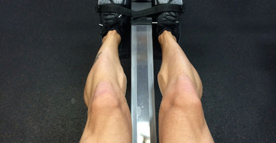 Person using a rowing machine at the gym, showing leg muscles engaged during a fitness and endurance workout.