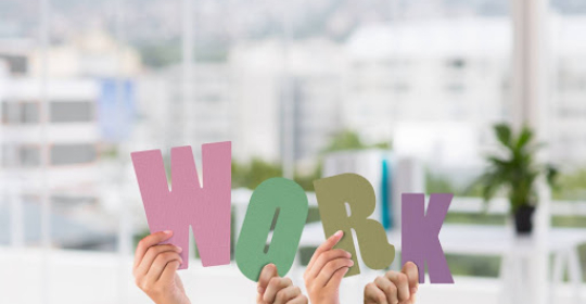 Employees holding colorful letters spelling “work,” symbolising teamwork and a positive workplace environment